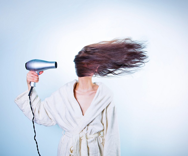 picture of woman with long hair wearing bathrobe and holding a hair drier in her hand on a blue background