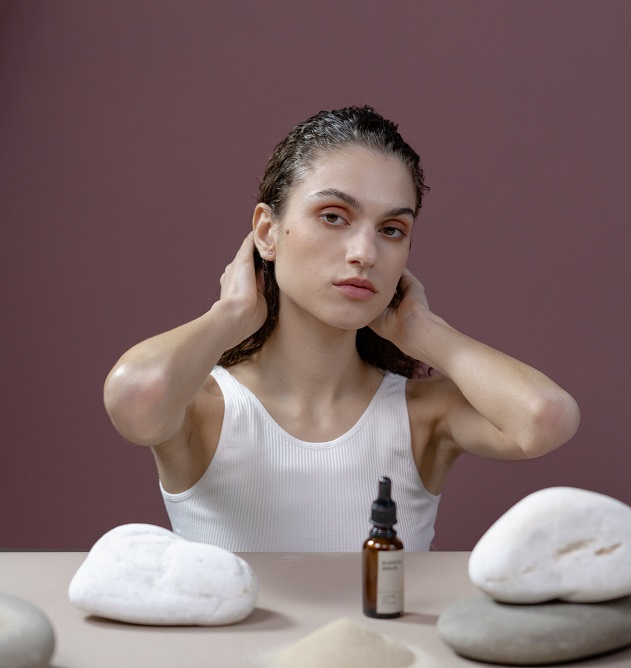 picture of a woman putting essential oil on her hair in front a purple background 