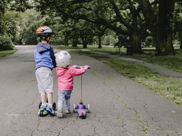 picture of two kids riding scooters in a park