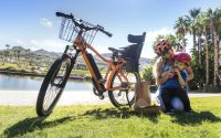 picture of woman with a baby boy beside a bicycle in a park beside water