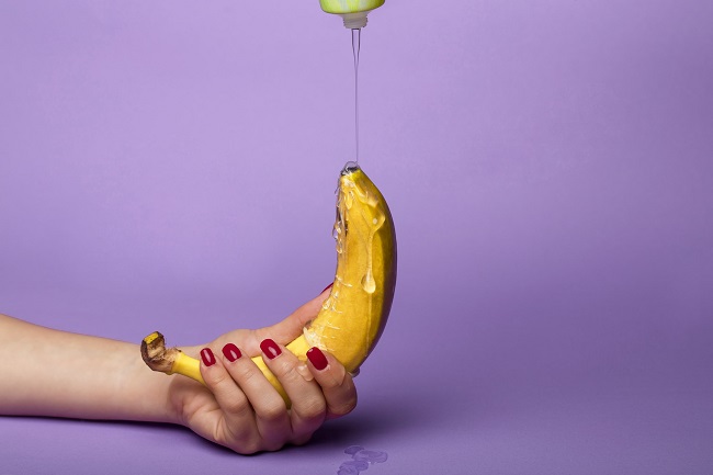 picture of a banana fruit on persons hand putting a silicone based lubricant on a purple background 