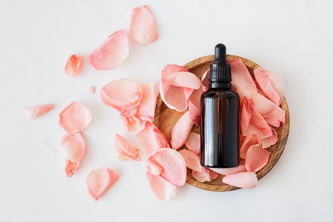 picture of a bottle in a wooden bowl full with pile of pink flower leaves on a white background  