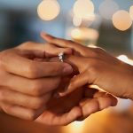 Closeup shot of a man putting an engagement ring onto his fiancee’s finger